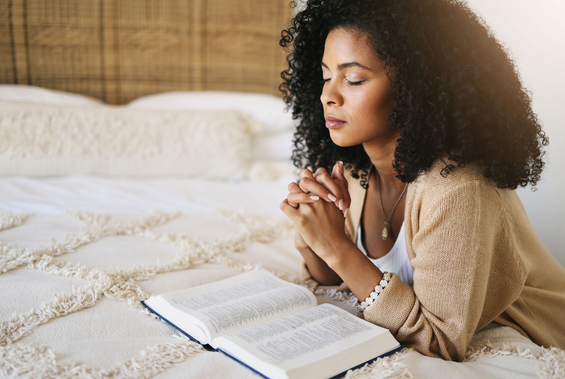 Bible, prayer and black woman praying on bed in bedroom home for hope, help or spiritual faith. God, christian and female worship Jesus or Holy Spirit for forgiveness, compassion or grace in house.